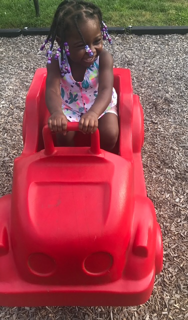 Young girl enjoying playground time in a red ride-on toy